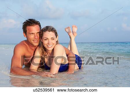Stock Image - Romantic Couple Lying In Sea On Tropical Beach Holiday. Fotosearch