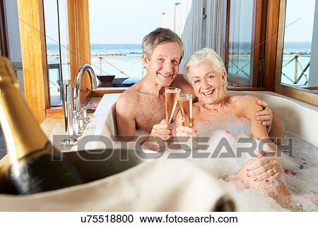 Stock Image - Senior Couple Relaxing In Bath Drinking Champagne Together. Fotosearch