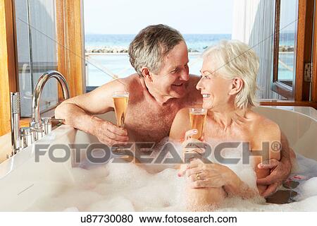 Stock Image - Senior Couple Relaxing In Bath Drinking Champagne Together. Fotosearch