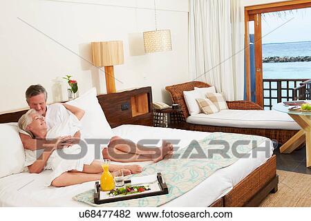Stock Image - Senior Couple Relaxing In Hotel Room Wearing Robes. Fotosearch