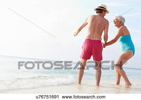 Stock Image - Senior Couple Splashing In Sea On Beach Holiday. Fotosearch