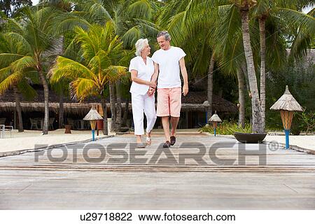 Stock Image - Senior Couple Walking On Wooden Jetty. Fotosearch