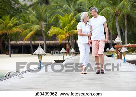 Stock Image - Senior Couple Walking On Wooden Jetty. Fotosearch