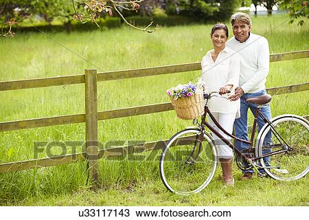 Stock Image - Senior Indian Couple On Cycle Ride In Countryside. Fotosearch