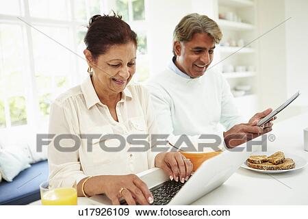 Stock Photo - Senior Indian Couple Using Laptop And Digital Tablet At Home. Fotosearch