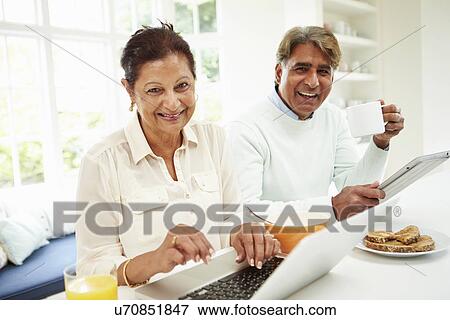 Stock Photo - Senior Indian Couple Using Laptop And Digital Tablet At Home. Fotosearch