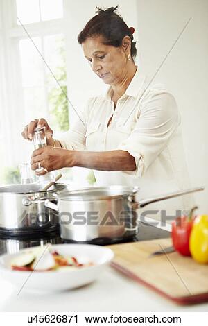Stock Image - Senior Indian Woman Cooking Meal At Home. Fotosearch