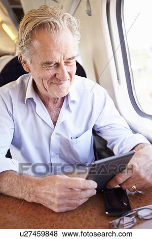 Stock Photo - Senior Man Reading E Book On Train Journey. Fotosearch