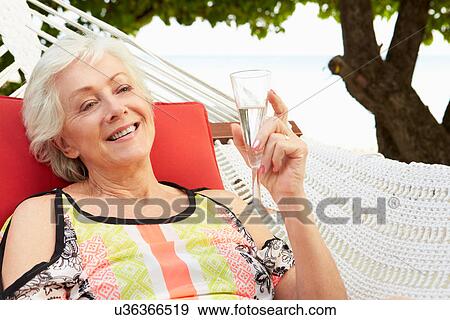 Stock Photo - Senior Woman Relaxing In Beach Hammock With Champagne. Fotosearch