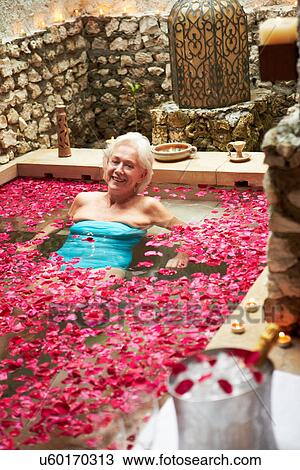 Stock Image - Senior Woman Relaxing In Flower Petal Covered Pool At Spa. Fotosearch