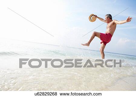 Stock Photo - Senior Woman Splashing In Sea On Beach Holiday. Fotosearch