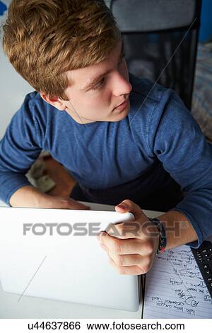 Stock Photograph - Teenage Boy Behaving Suspiciously Whilst Using Laptop. Fotosearch