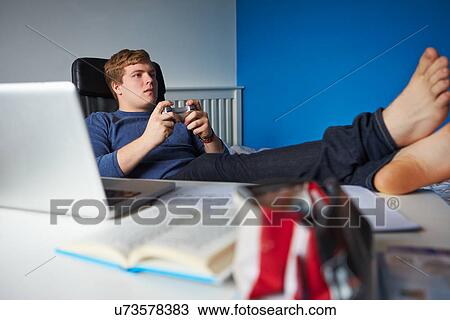 Stock Image - Teenage Boy Playing Video Game Instead Of Studying. Fotosearch