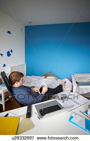 Stock Photo - Teenage Boy Sitting At Desk In Bedroom Using Digital Tablet. Fotosearch