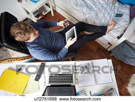 Teenage Boy Sitting At Desk In Bedroom Using Digital Tablet View Large Photo Image Stock Photo - Teenage Boy Sitting At Desk In Bedroom Using Digital Tablet. Fotosearch