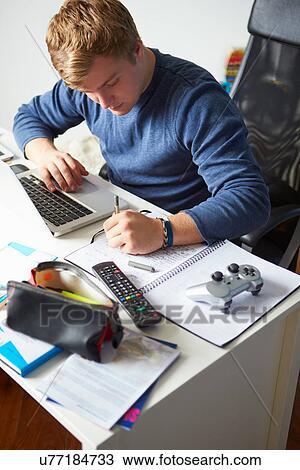 Stock Image - Teenage Boy Studying In Bedroom Using Laptop. Fotosearch