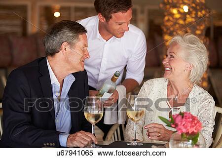 Stock Photography - Waiter Serving Wine To Senior Couple In Restaurant. Fotosearch