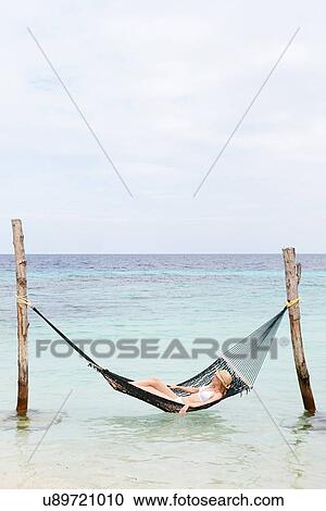 Stock Image - Woman Wearing Bikini And Sun Hat Relaxing In Beach Hammock . Fotosearch
