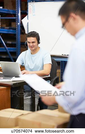 Picture - Worker In Warehouse Wearing Headset And Using Laptop. Fotosearch