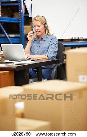 Stock Image - Worker In Warehouse Wearing Headset And Using Laptop. Fotosearch