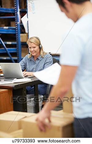 Stock Image - Worker In Warehouse Wearing Headset And Using Laptop. Fotosearch