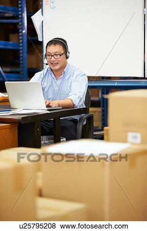 Worker In Warehouse Wearing Headset And Using Laptop View Large Photo Image Stock Photo - Worker In Warehouse Wearing Headset And Using Laptop. Fotosearch