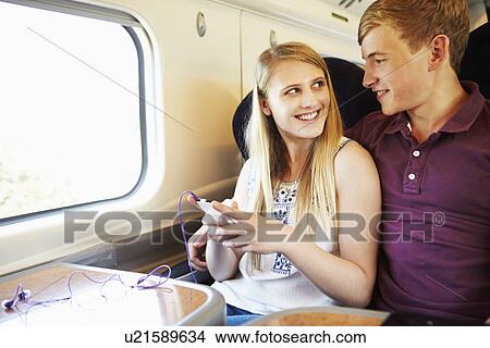 Picture - Young Couple Listening To Music On Train Journey. Fotosearch