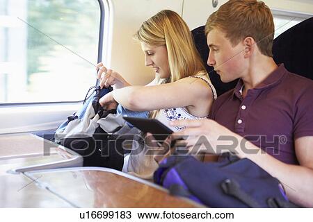 Stock Image - Young Couple Reading E Book On Train Journey. Fotosearch