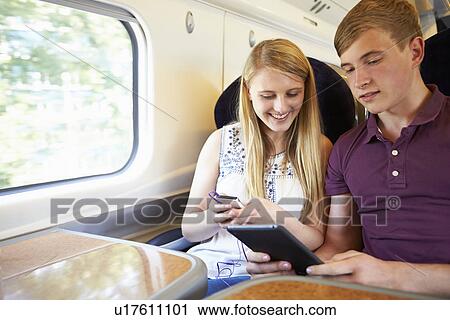 Stock Image - Young Couple Reading E Book On Train Journey. Fotosearch