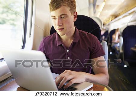 Stock Image - Young Man Using Laptop On Train Journey. Fotosearch