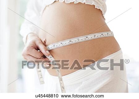Stock Image - Pregnant woman measuring her abdomen. Fotosearch
