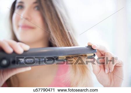 Stock Image - Woman using hair straighteners. Fotosearch