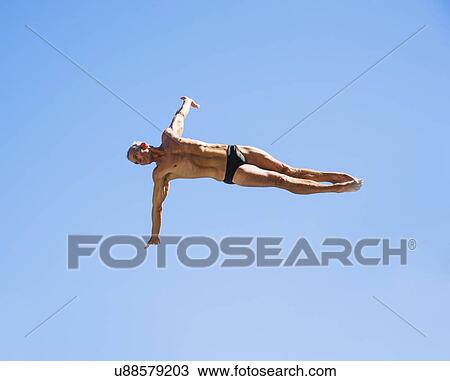 Stock Image - Athletic swimmer mid-air against blue sky. Fotosearch