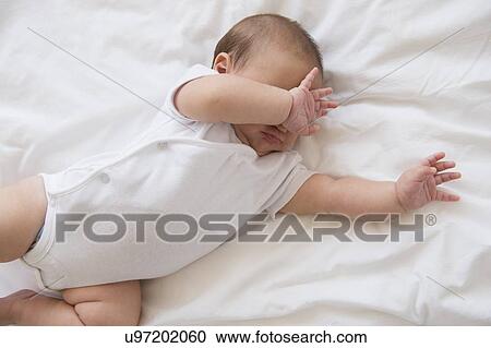 Stock Image - Baby girl (2-5 months) lying on bed and crying. Fotosearch
