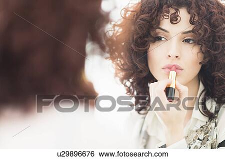 Stock Photograph - Beautiful brunette woman applying lipstick. Fotosearch