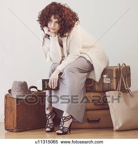 Stock Photography - Beautiful brunette woman sitting on suitcases. Fotosearch