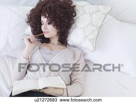Stock Image - Beautiful woman lying in bed holding diary. Fotosearch