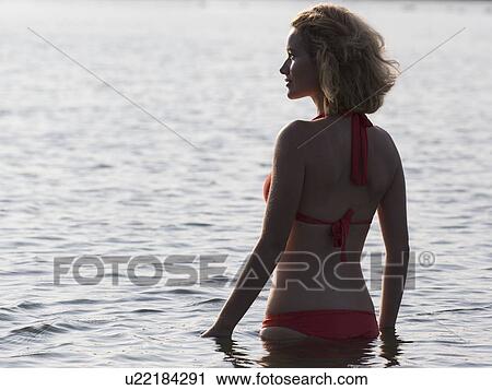 Stock Image - Beautiful woman standing in lake at sunrise. Fotosearch