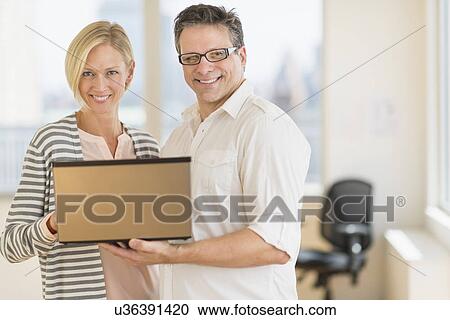 Business man and woman holding laptop View Large Photo Image Stock Image - Business man and woman holding laptop. Fotosearch
