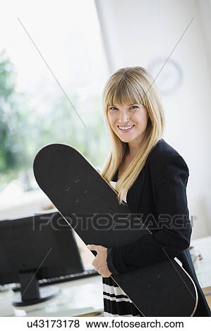 Businesswoman holding skateboard in office View Large Photo Image Stock Photo - Businesswoman holding skateboard in office. Fotosearch