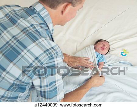 Stock Photo - Father wrapping newborn son (0-11 months) in blanket. Fotosearch