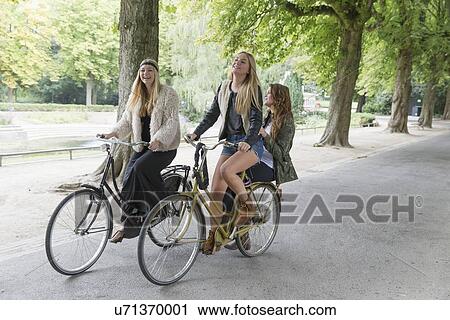 Stock Image - Female friends riding bike in park. Fotosearch