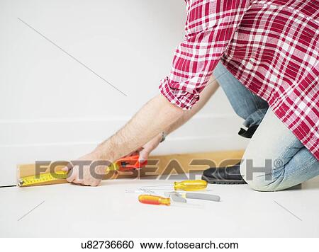 Stock Image - Man measuring baseboard. Fotosearch