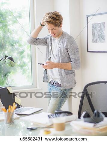Stock Image - Man using phone in home office. Fotosearch