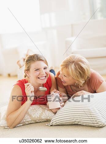 Stock Image - Mother and adult daughter relaxing at home, eating ice cream. Fotosearch