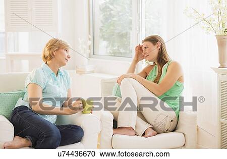 Stock Image - Mother and adult daughter sitting on sofa and talking. Fotosearch