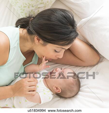 Mother and baby (2-5 months) lying on bed View Large Photo Image Picture - Mother and baby (2-5 months) lying on bed. Fotosearch