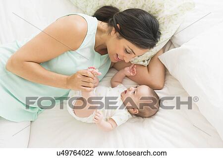 Stock Image - Mother and baby (2-5 months) lying on bed. Fotosearch