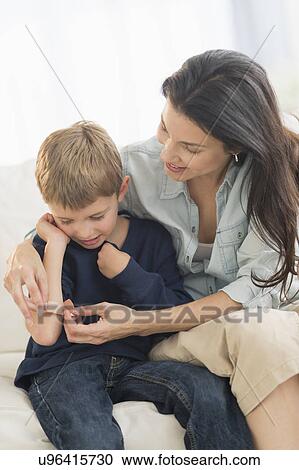 Stock Image - Mother helping son (6-7) put on bandaid. Fotosearch