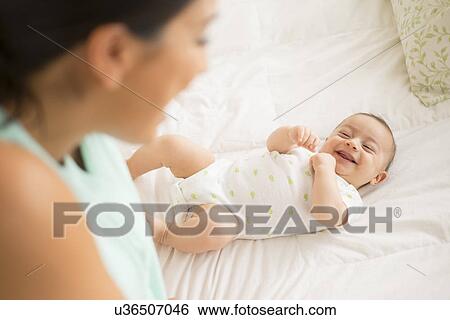 Stock Photograph - Mother looking at baby (2-5 months) lying on bed. Fotosearch